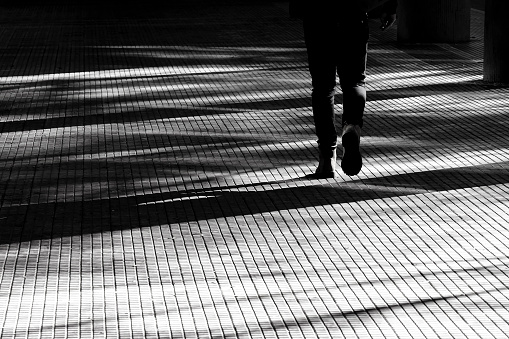 Blurry silhouette shadow of a legs of a person walking on a city arcade walkway in black and white high contrast