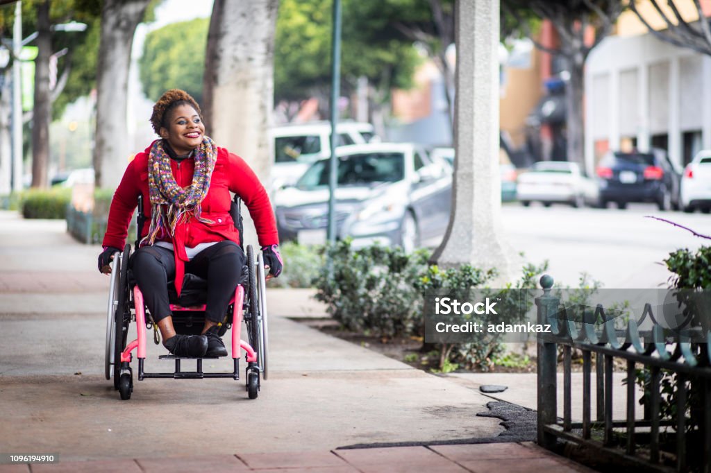Portrait of a Young Black Woman in a Wheelchair A young black disabled woman with a wheelchair and a bright colored sweater and her Asian friend walk around the city. Wheelchair Stock Photo