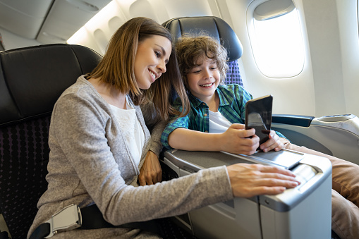 Happy mother and son traveling by plane and taking a selfie with a cell phone while smiling - travel concepts