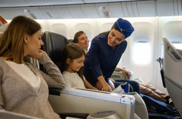 Portrait of a friendly flight attendant helping a girl in an airplane and looking very happy - travel concepts