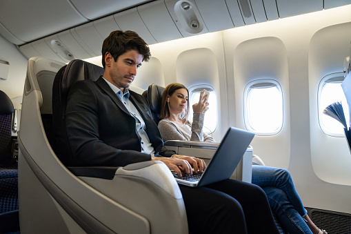 Portrait of a business man traveling by plane and working on his laptop computer - business trip concepts