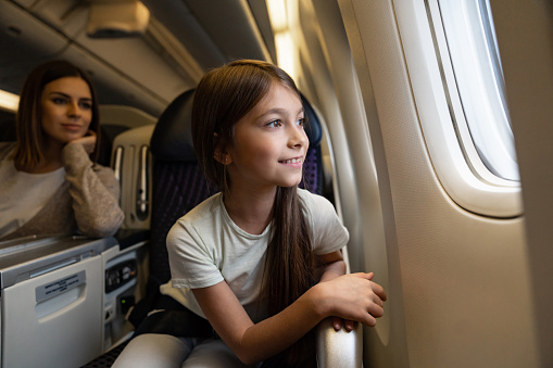 Portrait of a happy girl traveling by plane and looking through the window while smiling - travel concepts