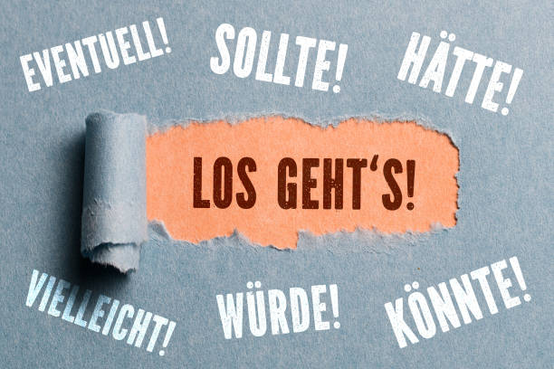 torn paper revealing command "let's go" to procrastinating words surrounding the hole (in German) stock photo