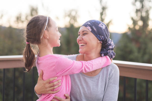 Mother with cancer hugging her daughter A young mother fighting cancer and wearing a head scarf hugs her daughter and smiles at her deeply as they share a few moments of tranquility together outdoors on a deck. food chain stock pictures, royalty-free photos & images