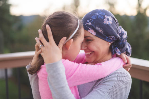 Mother with cancer hugging her daughter A young mother fighting cancer and wearing a head scarf hugs her daughter and smiles at her deeply as they share a few moments of tranquility together outdoors on a deck. Their faces are pressed together. behavior femininity outdoors horizontal stock pictures, royalty-free photos & images