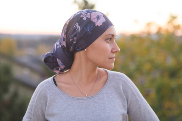 woman battling cancer stands outside and contemplates her life A beautiful young woman wearing a head wrap looks off-screen right and smiles pensively. She is standing outdoors and there are mountains and trees in the background. brest cancer hope stock pictures, royalty-free photos & images
