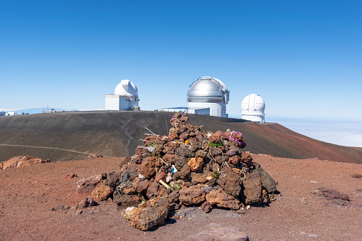Stunning view of a religious stone shrine on the summit of Mauna Kea volcano (4205 m) on the Big Island of Hawaii. Astronomical observatories in the background. Famous tourist destination.