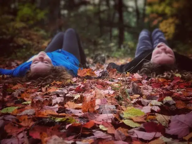 Photo of Two sisters in the woods, on the forest floor, playing and having outdoor fun.