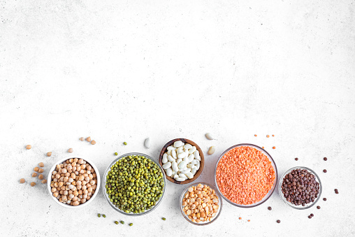 Assortment of colorful legumes in bowls, lentils,  kidney beans, chickpeas, mung, peas on white background, top view, copy space. Healthy food, dieting, nutrition concept, vegan protein source.