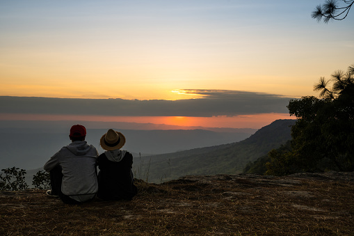 Image of sunset or sunrise on orange and yellow horizon with a silhouette of a couple in natural surrounding