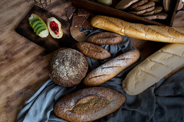 istock Breakfast and baked bread concept. Fresh fragrant bread and egg on wooden table. Fresh bread and coffee and wheat on wood black background. Kiwi and chocolate. Sesame seeds in the dish. 1096366152