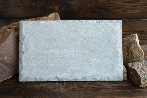 rectangular concrete plate on the background of granite stones. Dark wooden background.