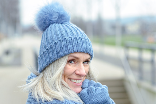 Attractive blue eyed blond woman in matching blue warm winter fashion wearing a knitted hat, scarf and gloves smiling at the camera