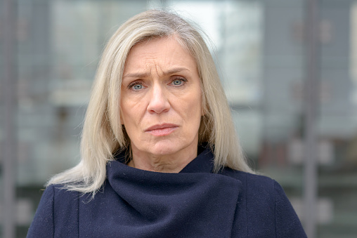 Puzzled troubled attractive middle-aged woman standing in an urban street frowning at the camera with an intent look