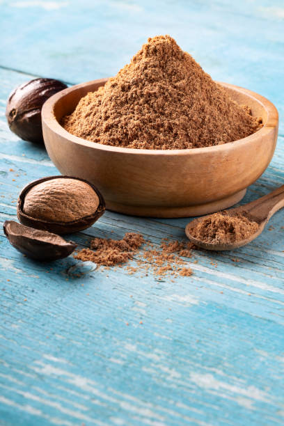 Whole inshell nutmeg nuts in a bowl on blue rustic wooden table.