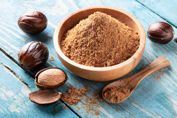 noci di noce moscata in guscio intero in una ciotola su tavolo di legno rustico blu. - nutmeg india spice nut foto e immagini stock