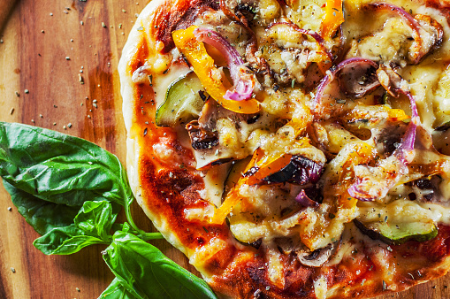 vegetarian pizza with Mozzarella cheese, grilled zucchini, mushrooms, red onion, pepper and fresh basil. Italian pizza on wooden table background