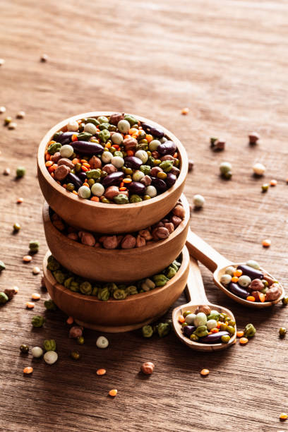 Mixed raw dried Indian legumes in wooden bowls on rustic background.
