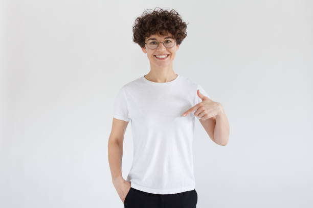 istock Young pretty woman smiling while pointing with index finger to white t-shirt, copyspace for advertising, isolated on gray background 1096419400