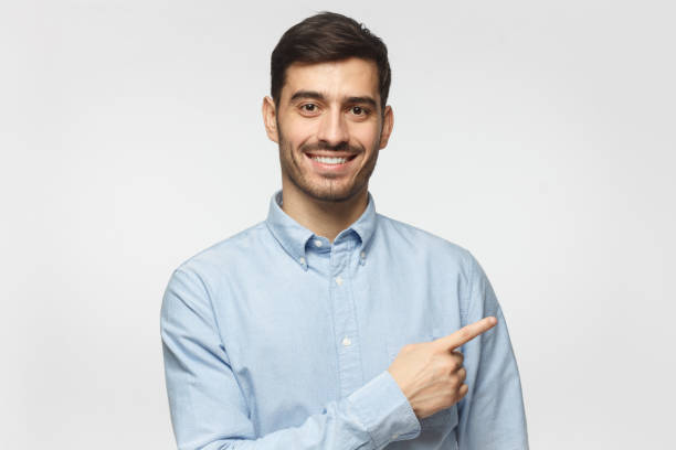 istock Smiling business man pointing right with index finger and looking at camera, isolated on gray background 1096419434