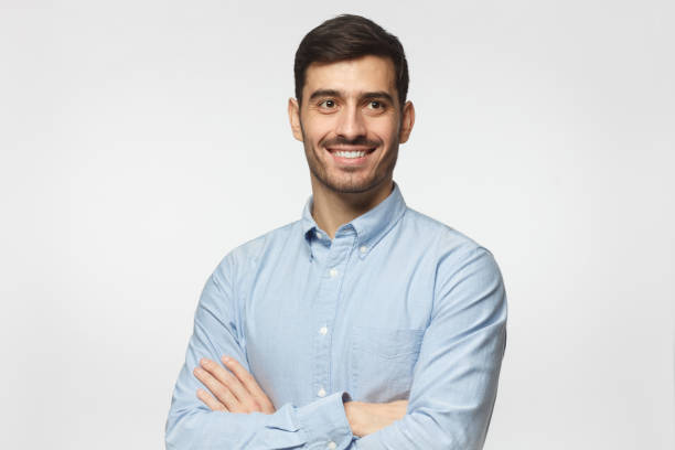 bello uomo d'affari sorridente in camicia blu in piedi con le braccia incrociate, isolato su sfondo grigio - crossing human arm leadership men foto e immagini stock