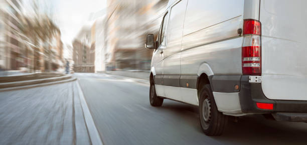 White transporter driving inside the city A fast moving white van on a bright street with high buildings. Motion blurred background. commercial land vehicle photos stock pictures, royalty-free photos & images
