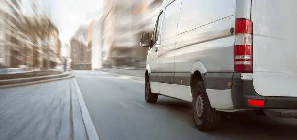 A fast moving white van on a bright street with high buildings. Motion blurred background.