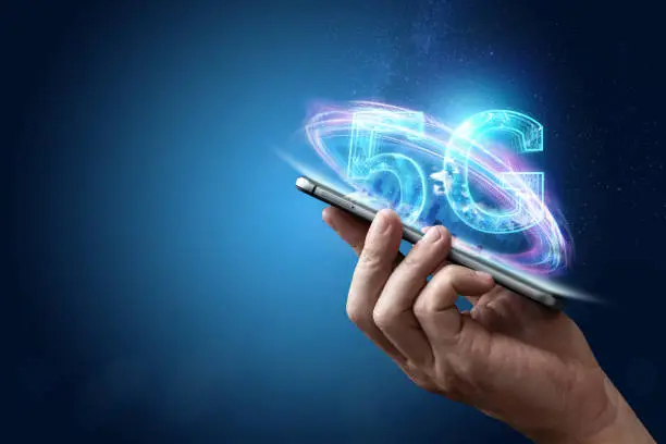 Photo of Creative background, male hand holding a phone with a 5G hologram on the background of the city. The concept of 5G network, high-speed mobile Internet, new generation networks. Copy space, Mixed media.