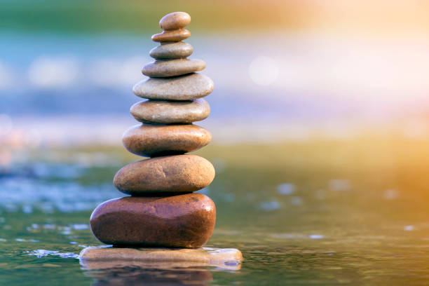 istock Close-up abstract image of wet rough natural brown uneven different sizes and forms stones balanced like pyramid pile landmark in shallow water on blurred blue-green misty copy space background. 1096449140