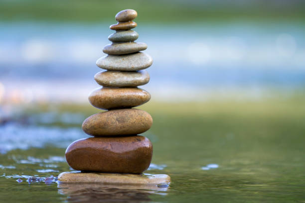 istock Close-up abstract image of wet rough natural brown uneven different sizes and forms stones balanced like pyramid pile landmark in shallow water on blurred blue-green misty copy space background. 1096454656