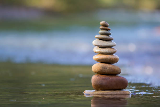 istock Close-up abstract image of wet rough natural brown uneven different sizes and forms stones balanced like pyramid pile landmark in shallow water on blurred blue-green misty copy space background. 1096454660