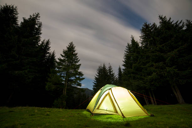 istock Summer camping at night. Illuminated tourist tent on green clearing on distant mountain background. 1096454726