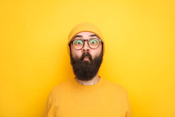 Childish hipster making faces at camera Bearded man in yellow outfit doing fish and looking expressively at camera on yellow background. funny fish lips stock pictures, royalty-free photos & images