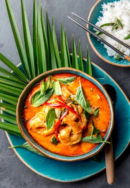 Photo of THAI SHRIMPS RED CURRY. Thailand Thai tradition red curry soup with shrimps prawns and coconut milk. Panaeng Curry in blue plate on gray background