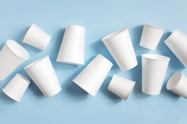 Various white disposable cups on the light blue background, top view