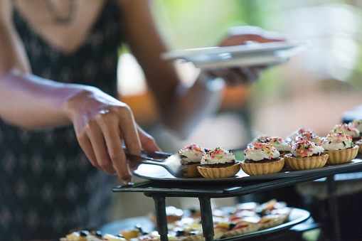 Unrecognizable woman taking desserts at buffet table