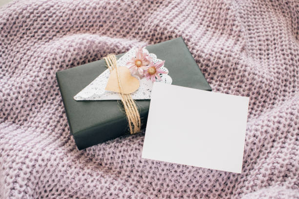istock Valentines day mockup. Craft gift box with empty white card on lilac knitted sweater. Black paper present box with heart, lace napkin, jute rope on knitted background. Love, romance concept 1096582536