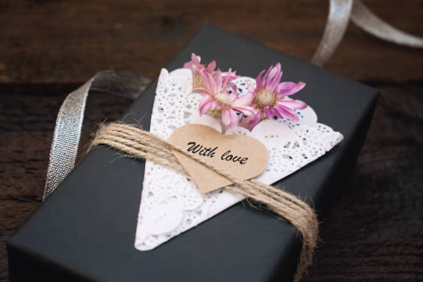 istock Valentines day craft gift box ideas. Black paper present box text WITH LOVE on heart, lace napkin, jute rope and silver on dark wooden background. Love, romance, handmade concept 1096582724