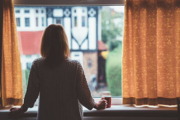 femme buvant du thé à la maison - regarder par la fenêtre photos et images de collection