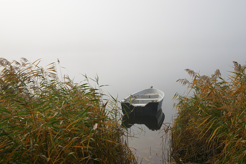 Boat floating on a calm misty lake. Masuria, Poland.