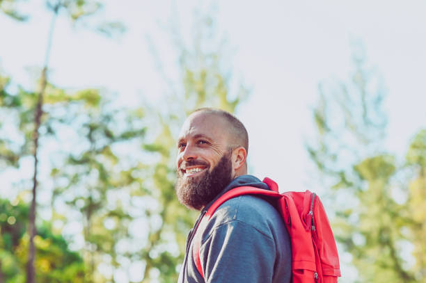 Handsome bearded man in his late 30’s hikes in a nature area, wearing a backpack. He has on a light jacket. Candid active outdoors, a natural environment
