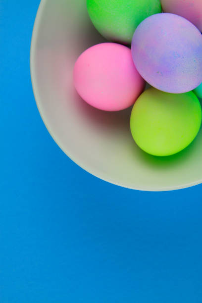 istock Overhead view of brightly painted easter eggs in a white bowl on blue background 1096625772