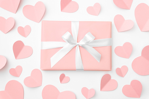 Valentine or women day coral gift box with bow ribbon decorated with pink or coral small hearts top view on white background. Concept decor love day or birthday. Flat lay.
