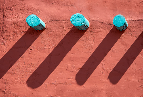 Background - Turquoise corbels and their long shadows on an orange stucco wall on southwestern style building