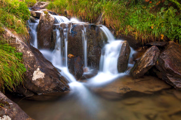 istock Beautiful little waterfall in mountains with white foamy water 1096653794