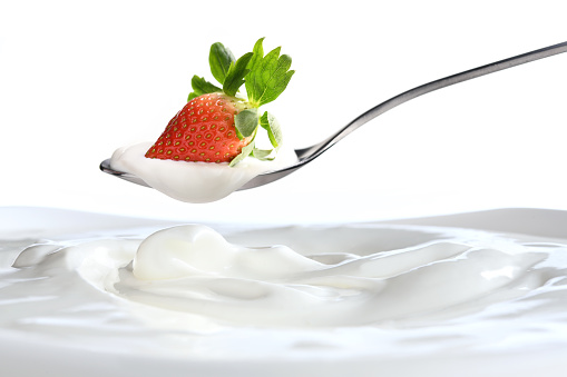 Plain yogurt on a spoon with fresh  strawberry on top hanging above of plain yogurt isolated on white background
