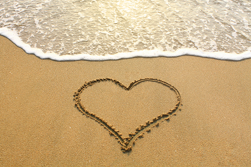 A heart-shaped painting on a sandy beach with a wave at sunset. Communication to lovers.