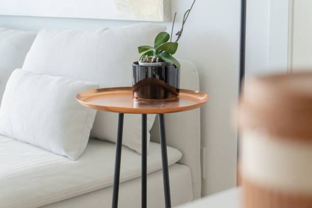 nowoczesny, miedziany stolik boczny, z czarnymi nogami, obok białej kanapy futon, skupiony w oddali, z rośliną doniczkową orchidei - side table zdjęcia i obrazy z banku zdjęć