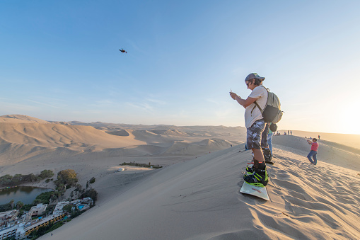 People sandboarding and flying drone in the desert of Huacachina in Peru, during the late afternoon in the summer.