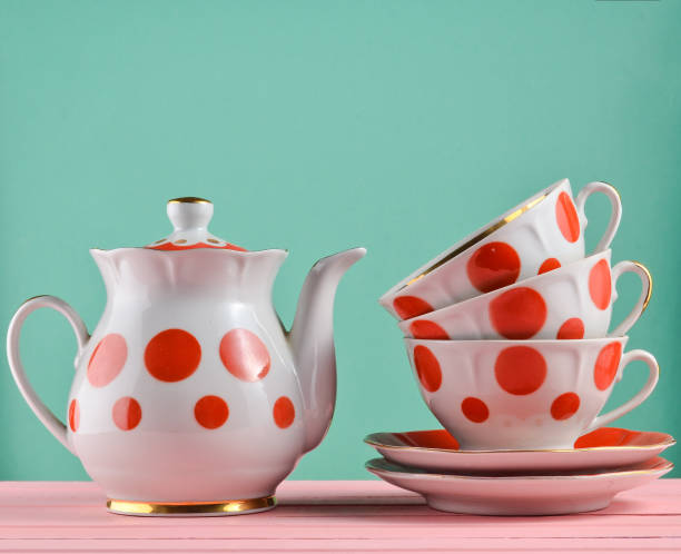 Ceramic teapot, a stack of cups in polka dots on a wooden table isolated on a blue pastel background. Copy space